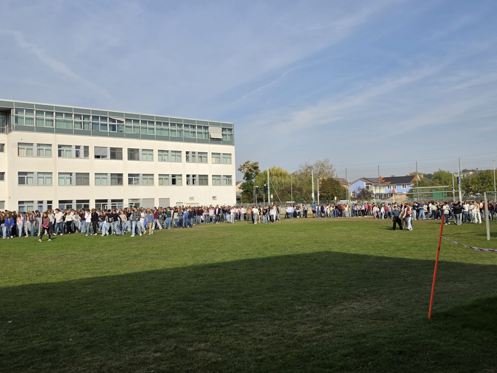 Schülerinnen und Schüler stehen vor einem Schulgebäude in einer Reihe auf einer Wiese